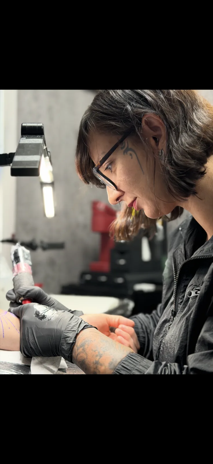 Juliana Farinazzo at work under the task lamp, glasses on, focused on the line