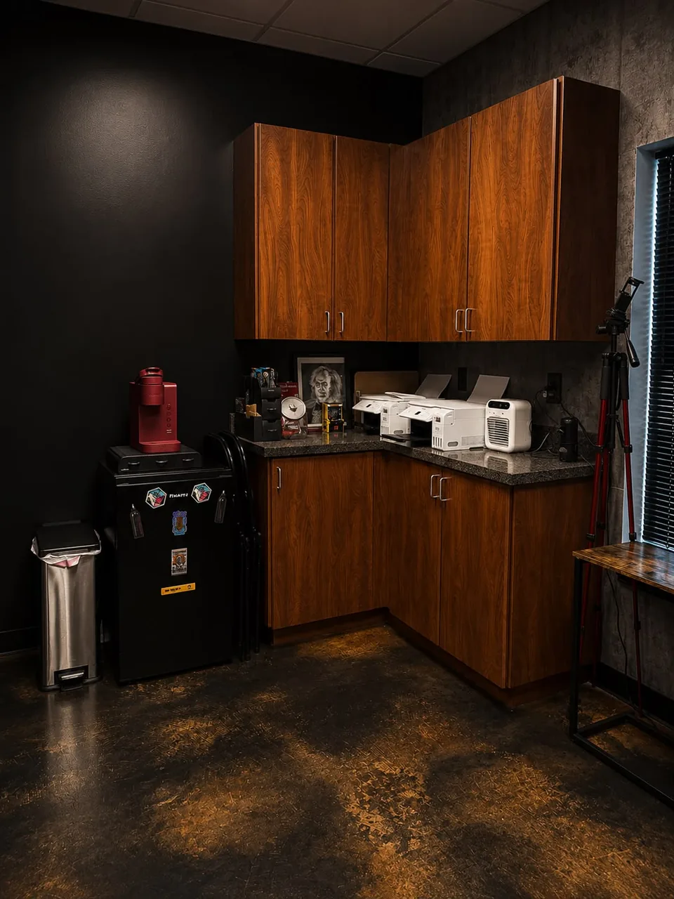 The back of the studio: wood cabinets, a counter with two printers, a coffee maker and a small fridge.